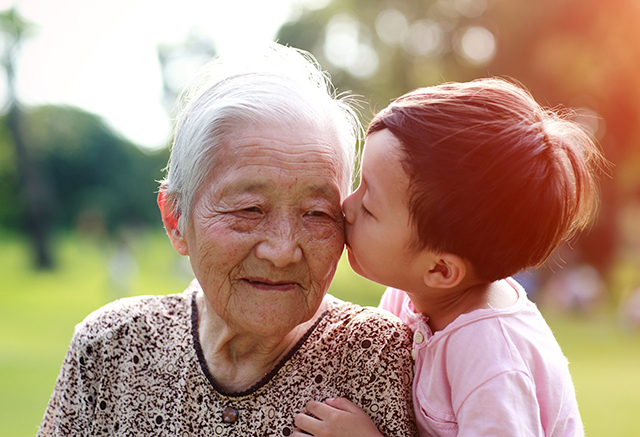 Happy Asian family Grandchild kissing their elderly grandmother on the cheek outdoors.