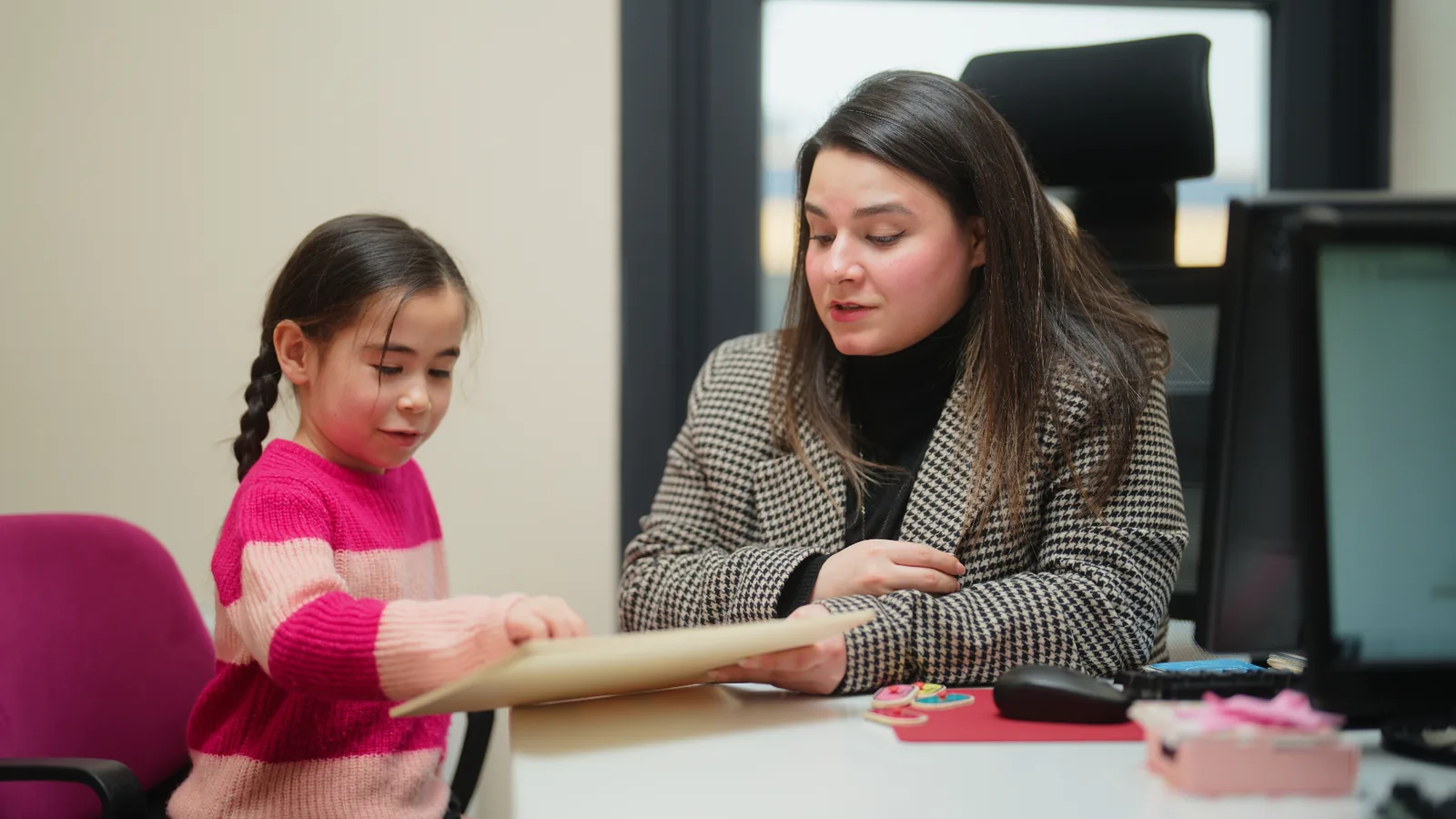 A solicitor sitting with a young child, looking through a drawing together in an office setting.